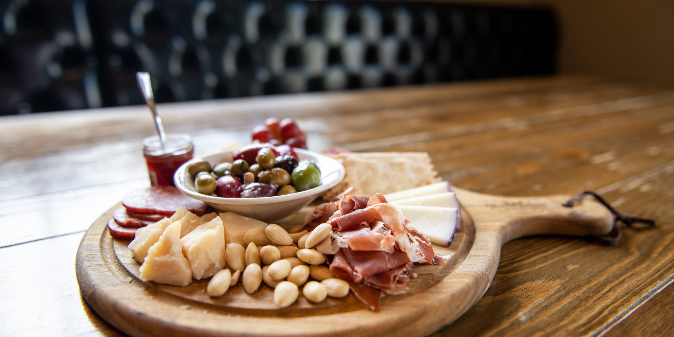 Charcuterie Board-4 Wooden charcuterie board with nuts, cheeses, meats, crackers, olives, and jam.